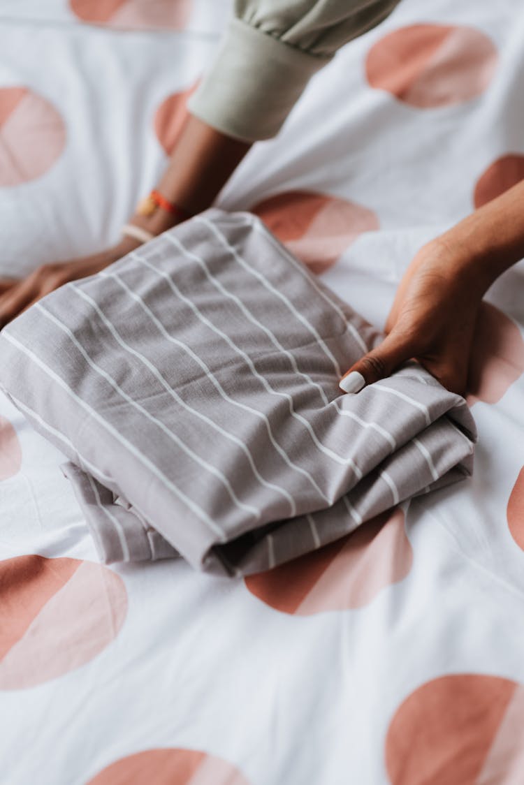 Crop Black Woman With Folded Clothes On Bed Blanket