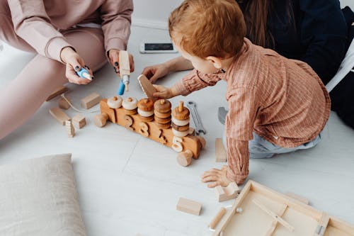 A Young Boy in Brown Long Sleeves Sitting on the Floor while Holding a Wooden Toys