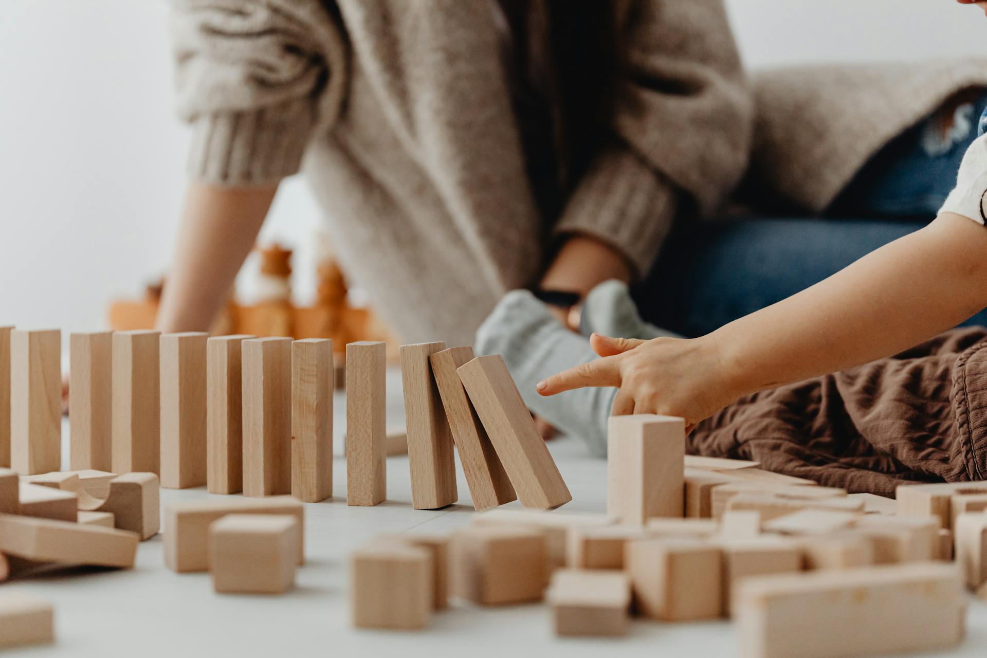 Close-up of child's hand tipping over wooden blocks on a table indoors.