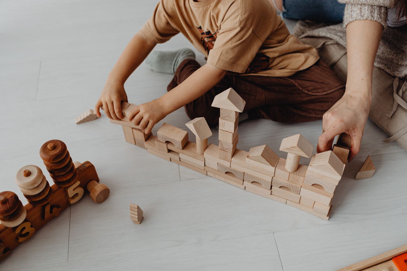 A child and an adult building together with wooden blocks on the floor.