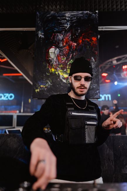 Energetic DJ spinning at a lively nightclub with colorful abstract art in the background.