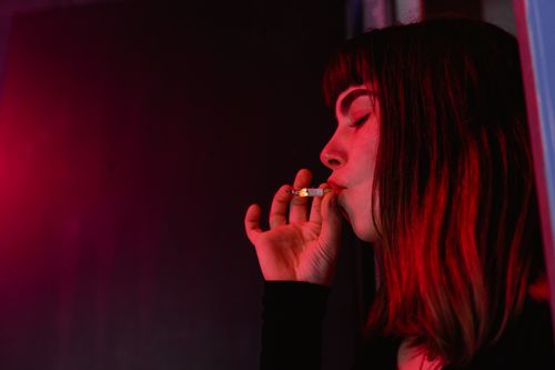 Free Close-up portrait of a woman smoking a cigarette under red lighting indoors. Stock Photo
