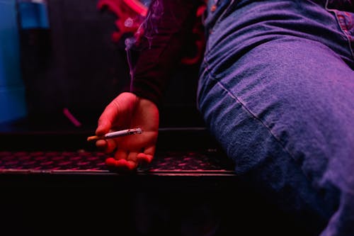 A Person in Blue Denim Jeans Holding a Cigarette