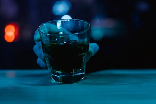A close-up shot of a hand holding a glass with a drink in a dimly lit bar setting.
