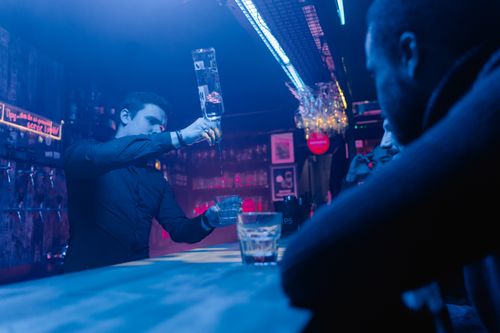 Free A bartender skillfully pouring drinks in a lively bar setting with patrons. Stock Photo