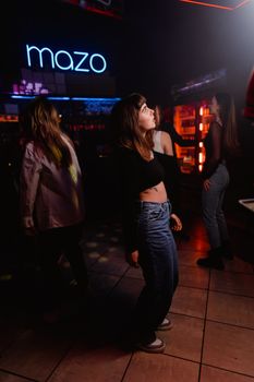 Group of young adults dancing in a vibrant nightclub with neon lights.