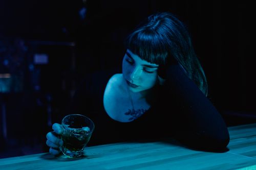 Free A woman with eyes closed holds a drink at a dim bar. Moody nightlife scene. Stock Photo