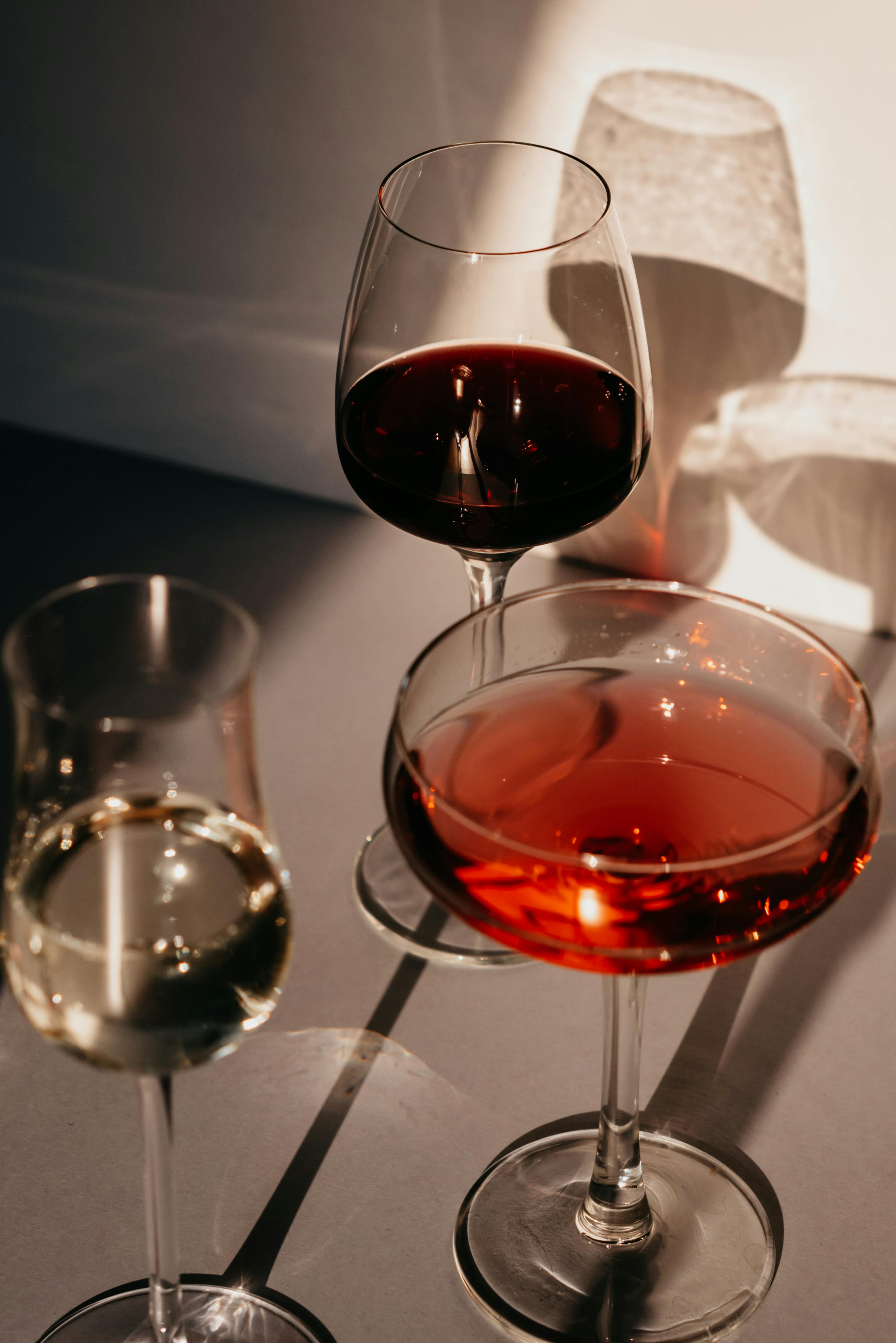 Three wine glasses with red, white, and rosé wine casting artistic shadows.