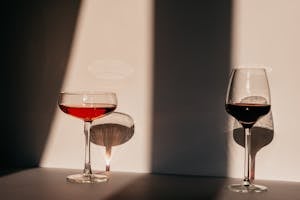 Red wine and vermouth in fragile glasses of various shapes arranged on table near white wall in sunlight