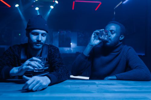 Free Two men enjoying drinks in a vibrant nightclub setting with blue lighting. Stock Photo