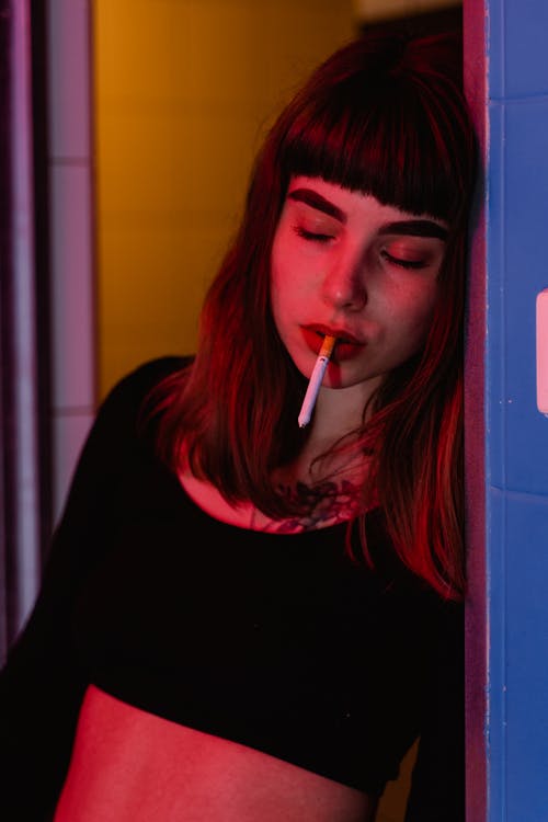 A Woman in Black Crop Top Leaning on the Wall with Cigarette on Her Mouth