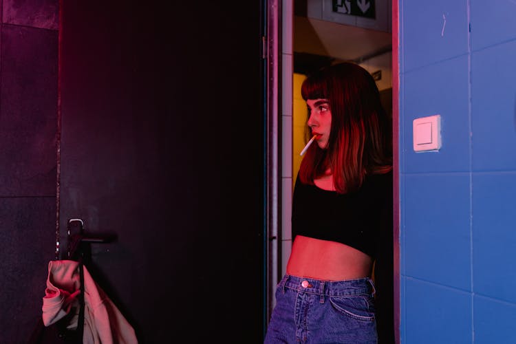 A Woman Standing Near The Door With Cigarette On Her Mouth