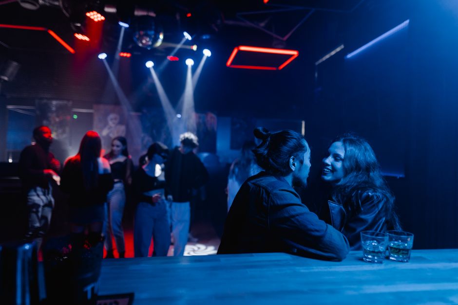 Young couple engaging in conversation at a vibrant nightclub with a lively atmosphere.