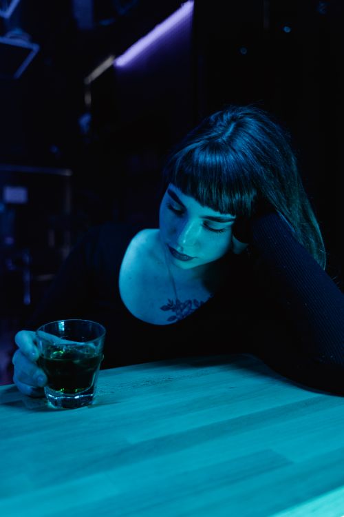 Free A woman ponders over a drink in a moody, neon-lit bar setting. Stock Photo