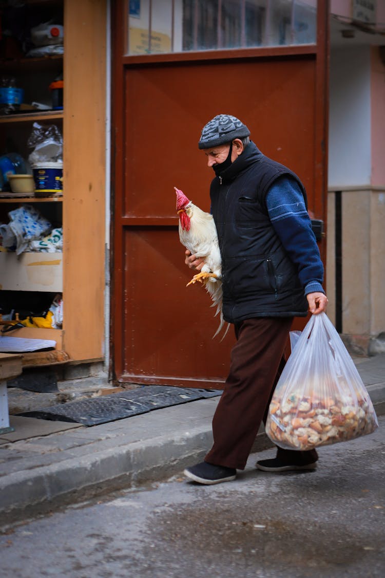 A Man Holding A Chicken And Plastic Bag