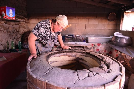 A woman bakes bread in a traditional stone oven in a rustic kitchen setting.