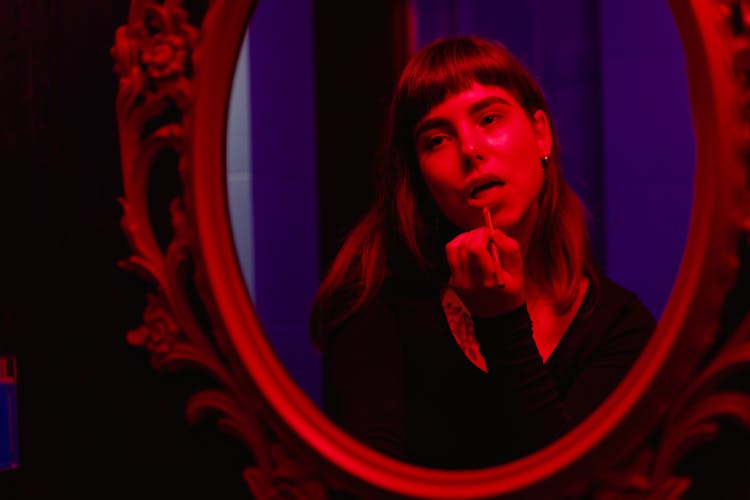 Woman In Black Long Sleeve Shirt Looking And Applying Lipstick On A Wall Mirror