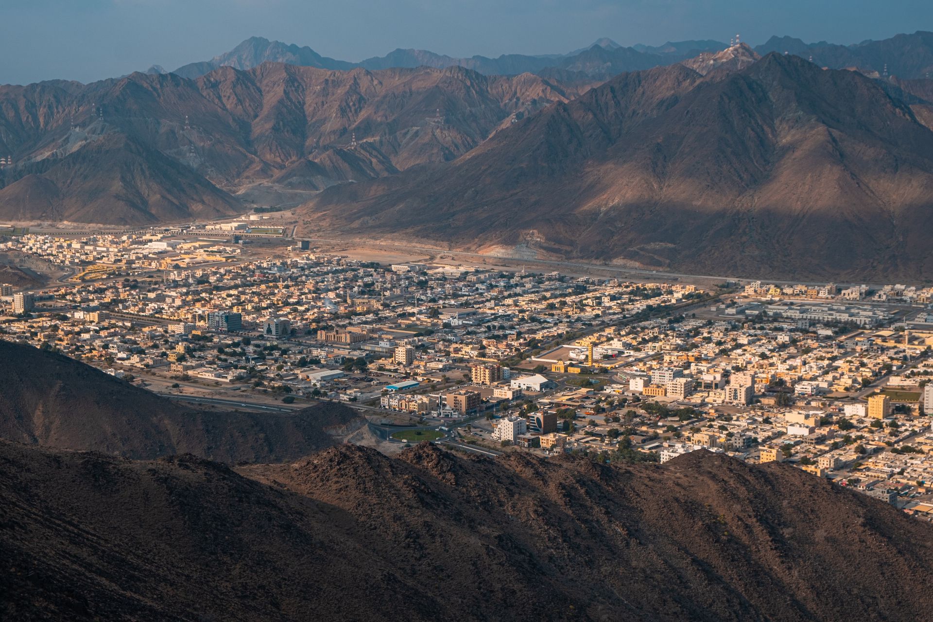 An expansive city nestled between rugged desert mountains under a clear sky in the UAE.