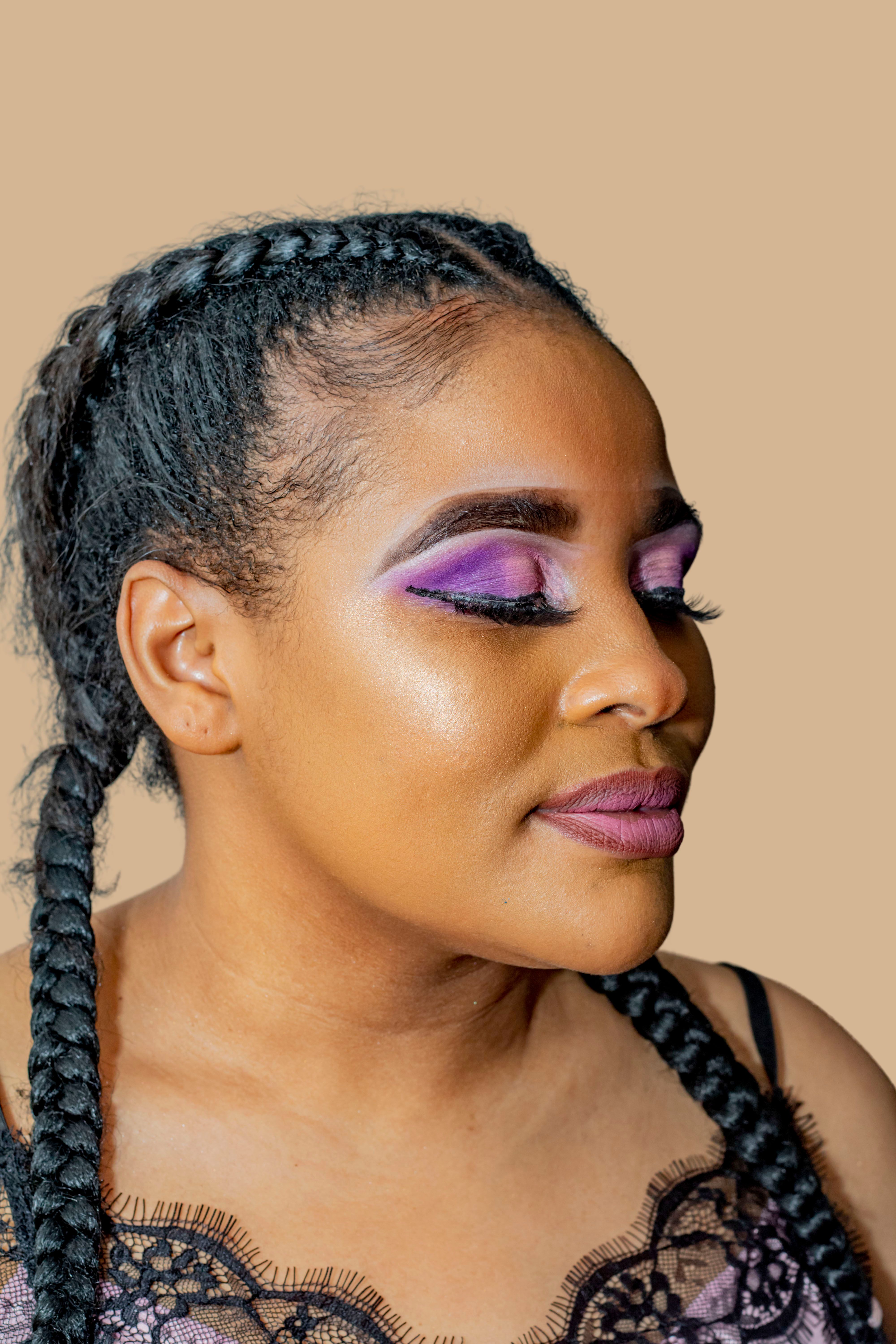 Close-up headshot of a young woman with purple eyeshadow and braided hair, exuding confidence.