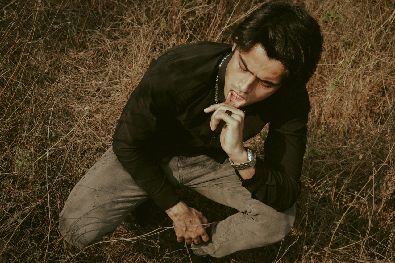 from above of ethnic male in chain and wristwatch pulling back lip whi