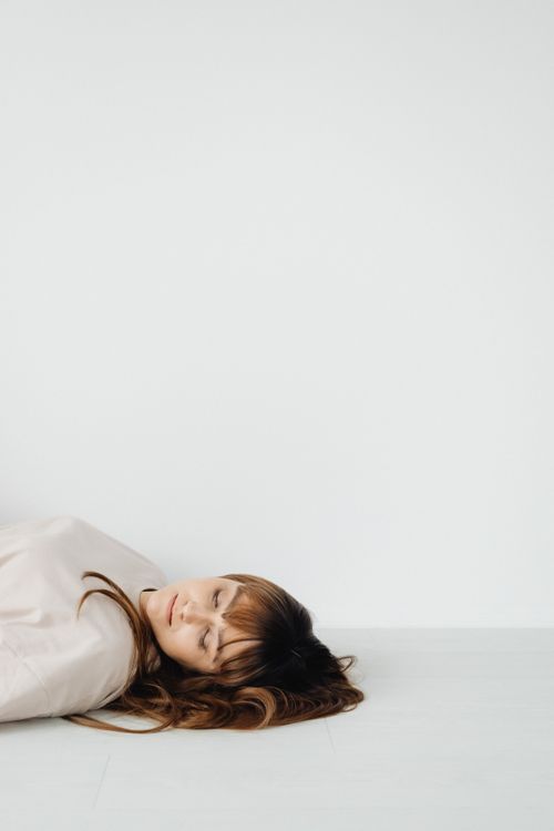 Free A serene woman with brown hair lying on a white floor, eyes closed. Stock Photo