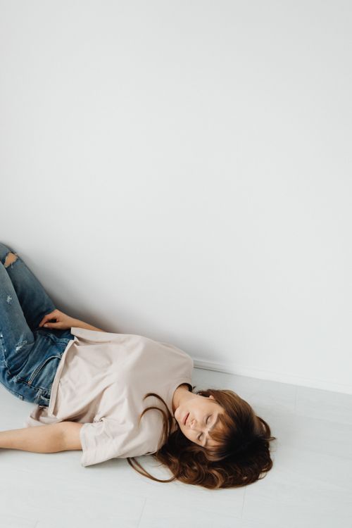 Free A brunette woman lies peacefully on a white floor, eyes closed, in casual attire against a minimalist backdrop. Stock Photo