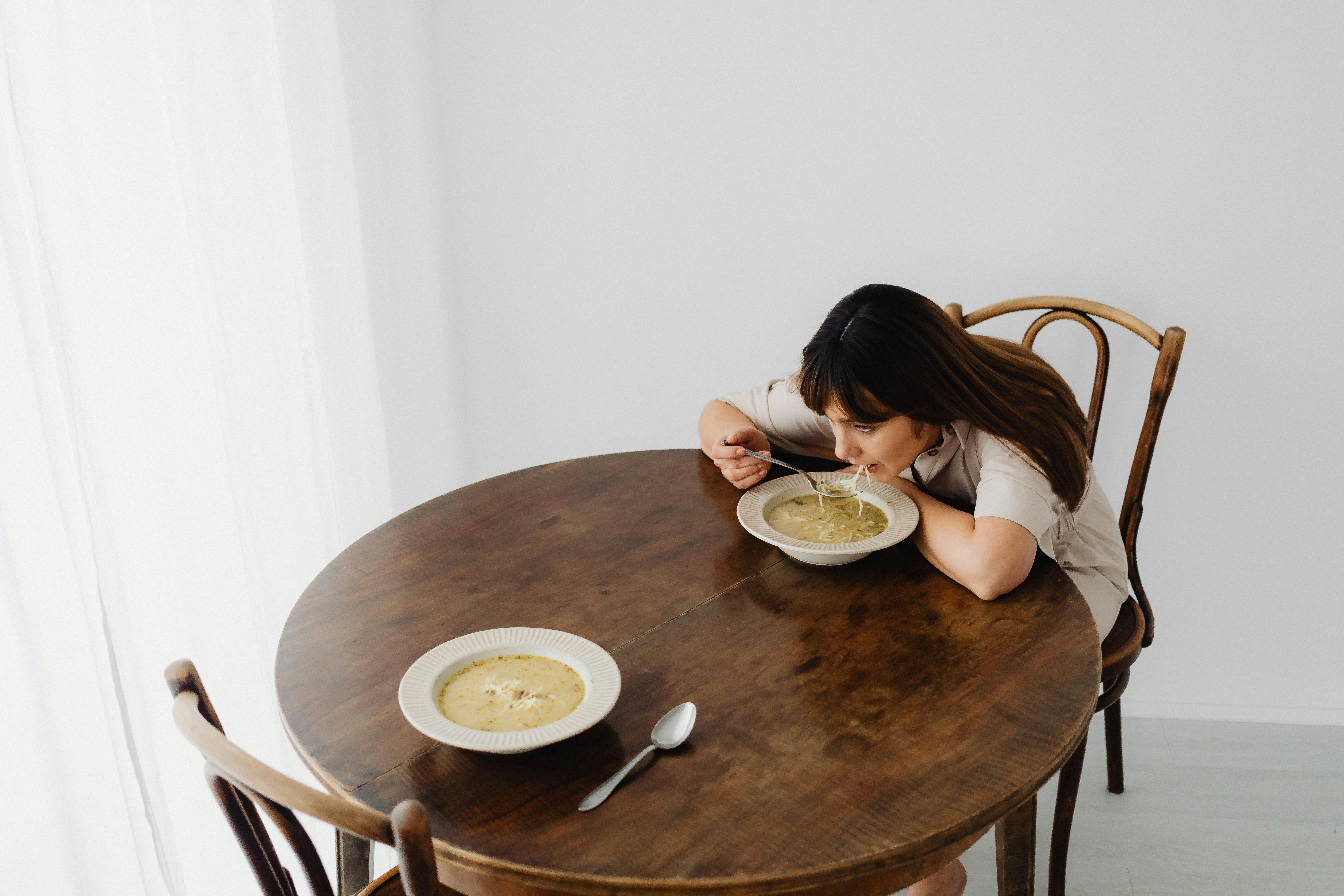 A woman sits alone savoring hot soup at a rustic table, creating a serene dining atmosphere.