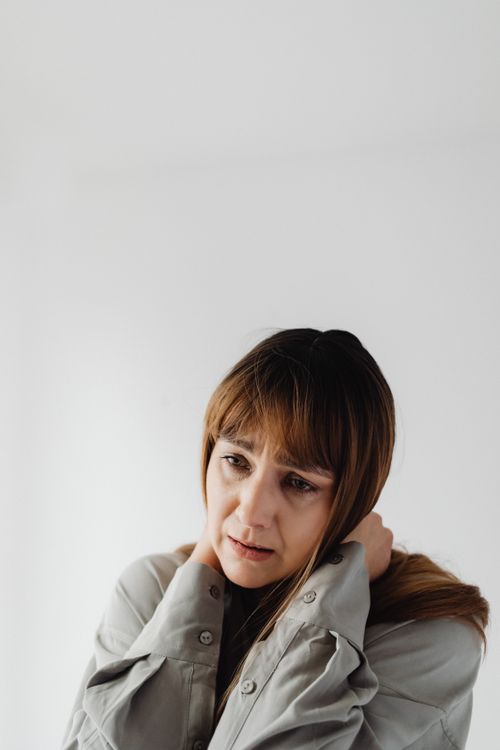 Free Portrait of a woman in gray with hands on neck, expressing worry and sadness. Stock Photo