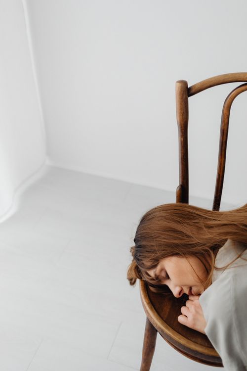 Free Serene portrait of a woman resting her head on a vintage wooden chair in a bright minimalist room. Stock Photo