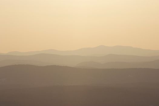 Peaceful dawn landscape with layers of misty mountain ranges under a warm glow.