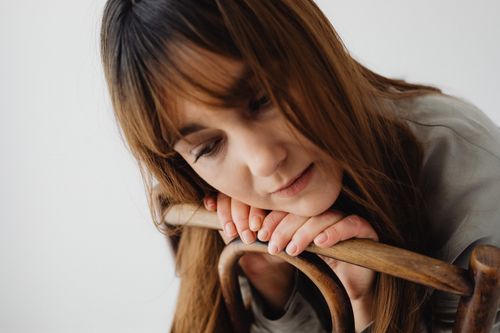 Free A woman with long brown hair leans thoughtfully on a wooden chair in a studio setting. Stock Photo