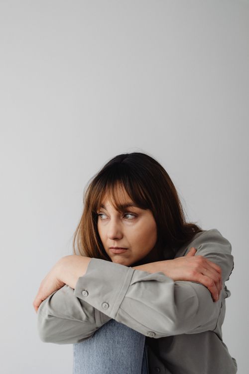 Free Pensive woman sitting with arms crossed on knees, looking contemplative. Stock Photo