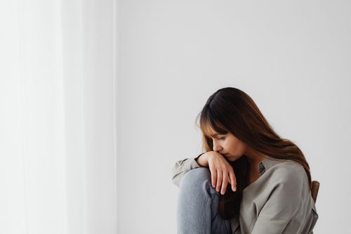 Free Woman sitting indoors, looking down with hand on knee, reflecting emotions. Stock Photo