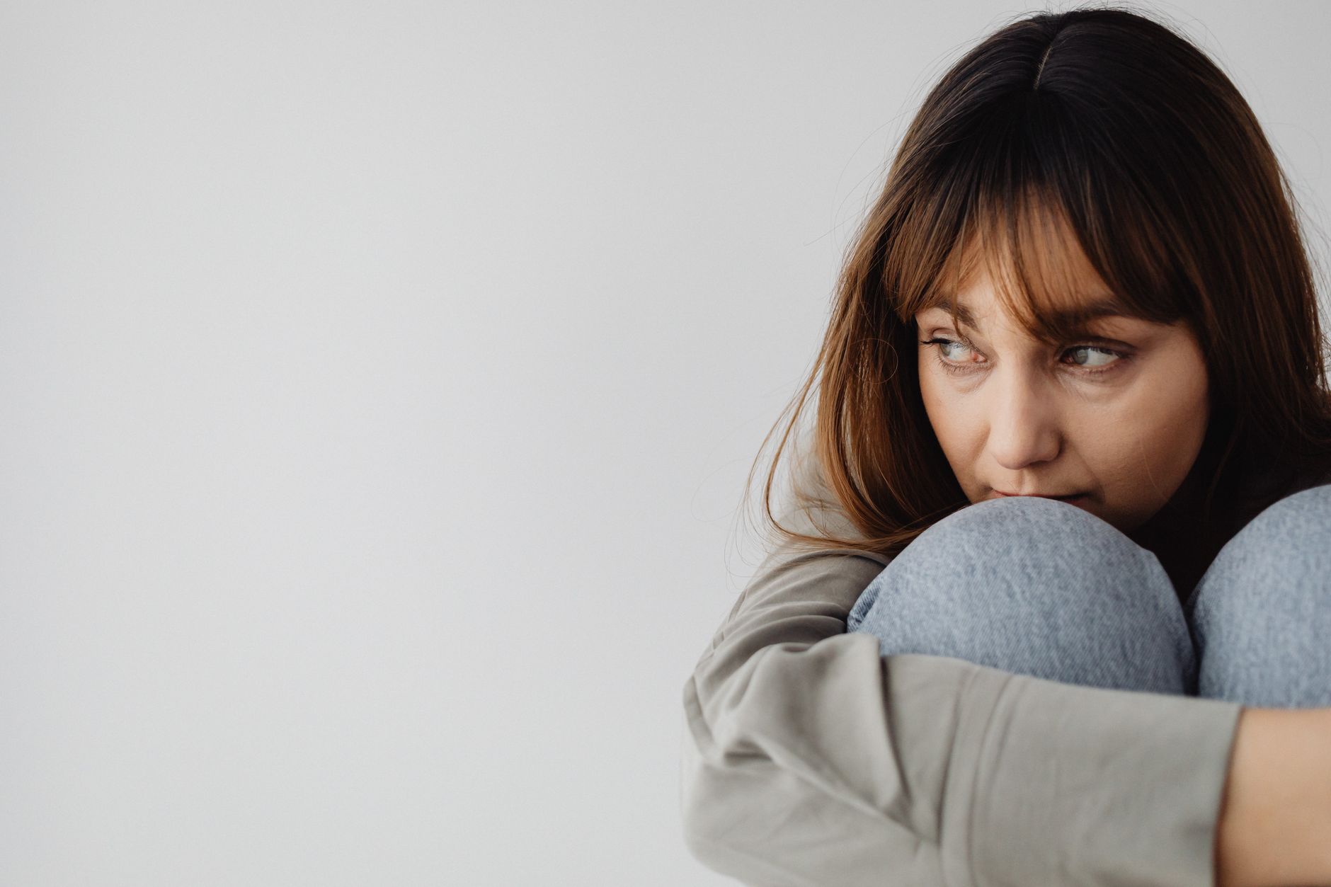 Close-up of a woman hugging her knees, gazing thoughtfully indoors