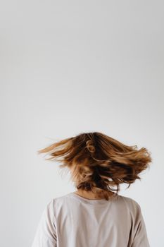 A woman with long hair swirling around, captured from the back against a plain white background.