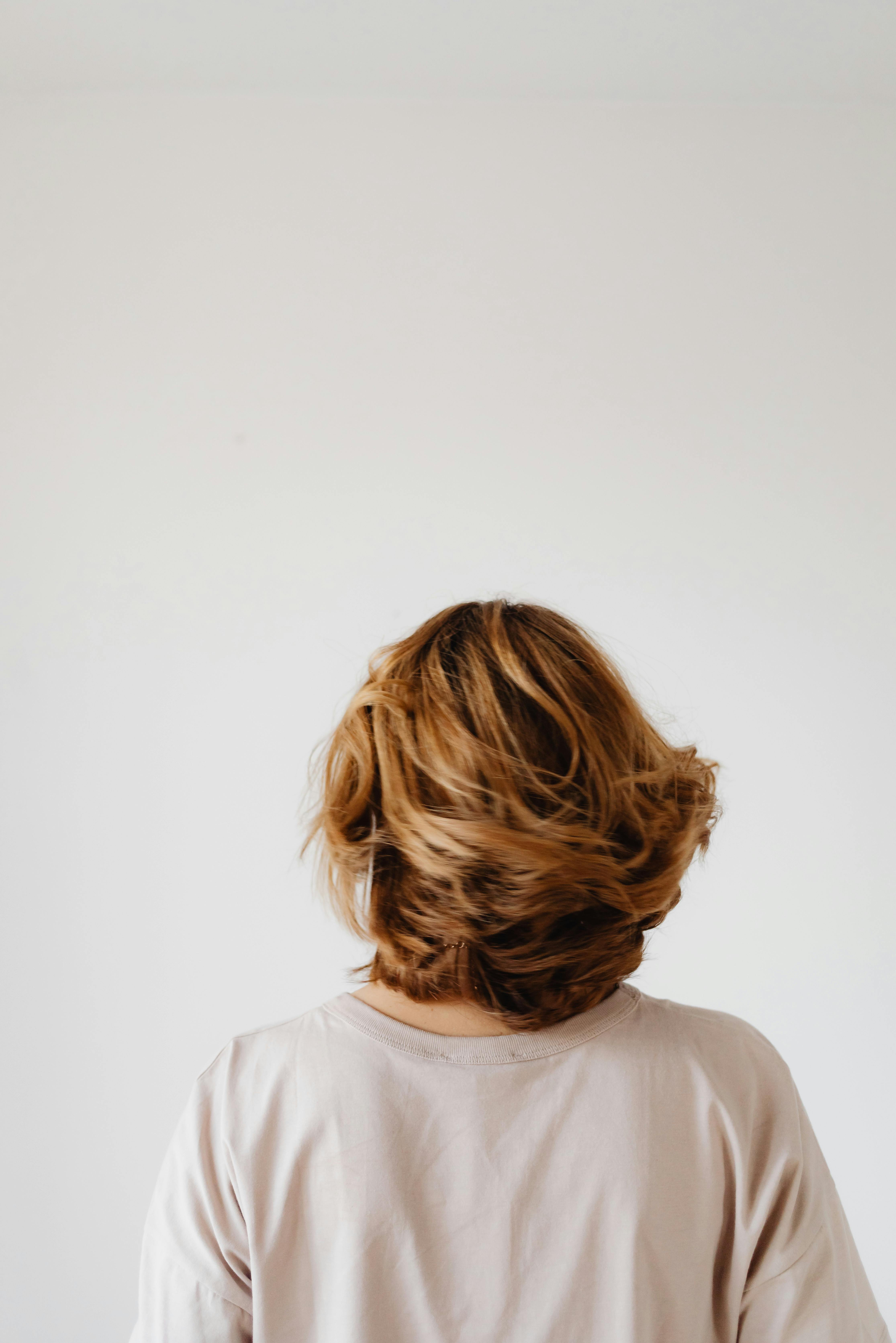 A back view of a woman with short blonde hair against a plain white backdrop, offering ample copy space.