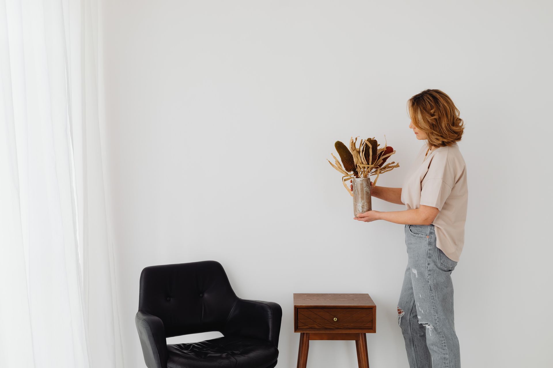 A woman arranges a dried floral bouquet in a contemporary living room setting.