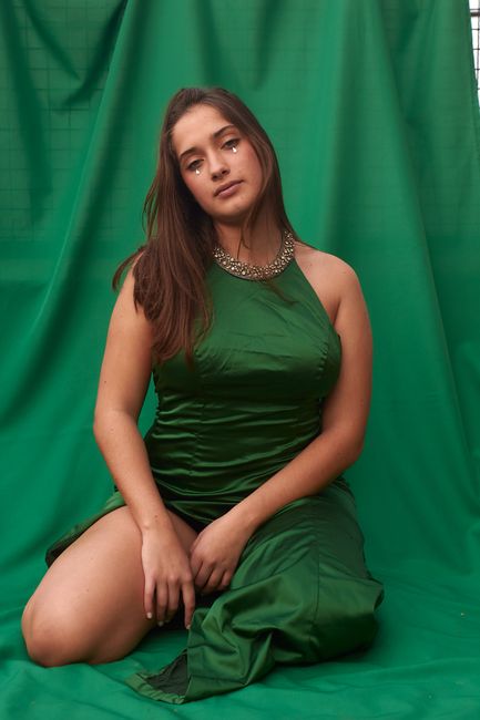 Portrait of a woman in a stylish green satin dress with a beaded necklace and relaxed pose.