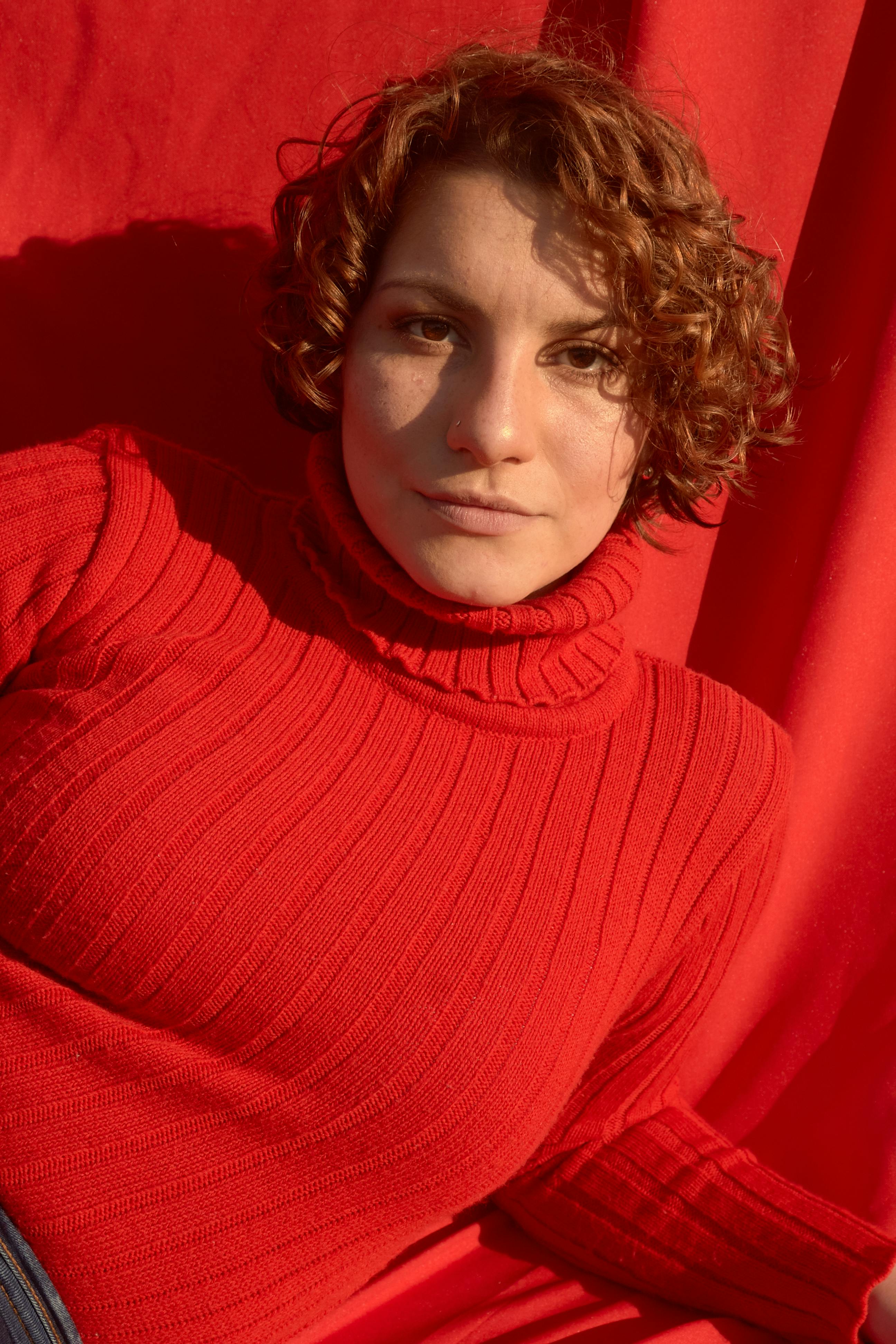 Vibrant portrait of a woman with red hair in a red turtleneck, set against a red background.