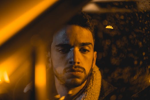 Close-up portrait of a man at night with rain drops on a window creating a moody ambiance.