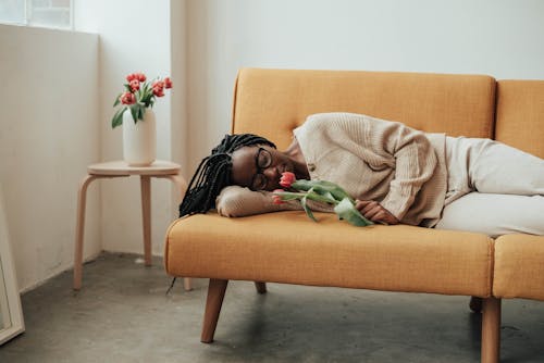 Calm African American woman with braided hair smelling tulips while lying along on couch at home