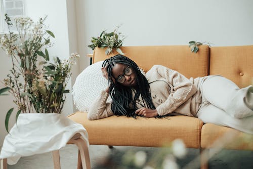 Serious African American woman on couch near plants and flowers