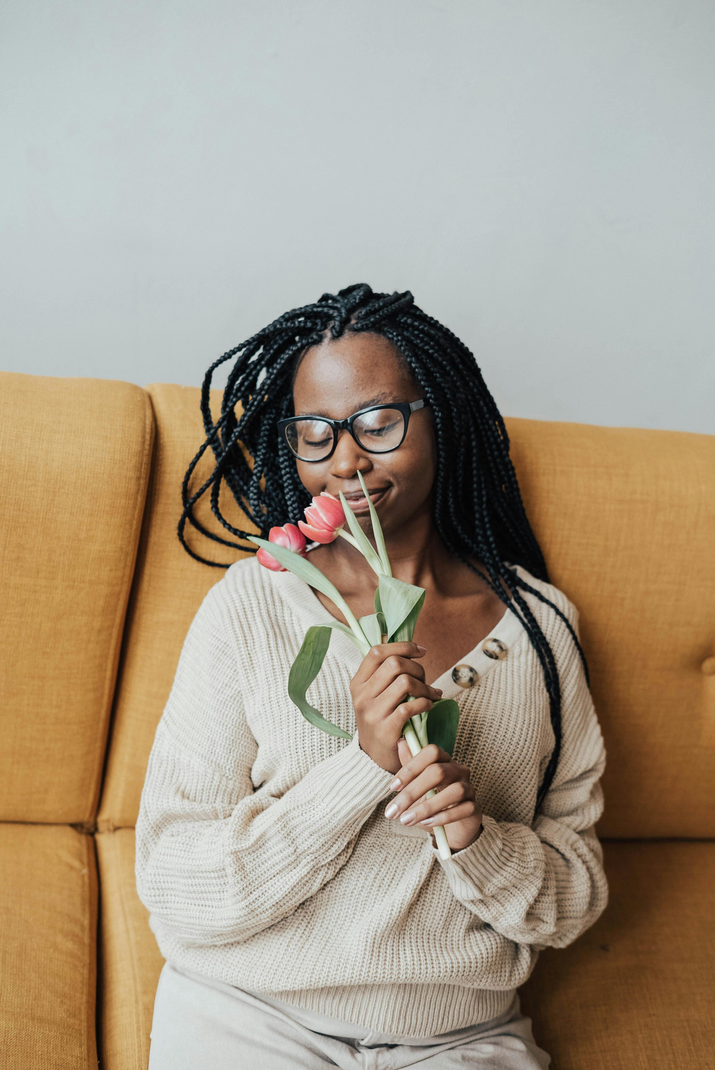 smiling african american woman on couch smelling flowers