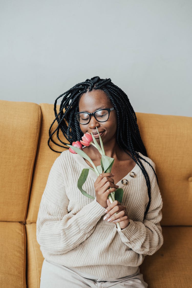 Smiling African American Woman On Couch Smelling Flowers