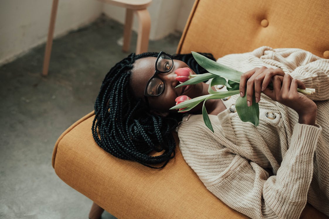 Free Positive black lady with flowers in hands lying on sofa Stock Photo