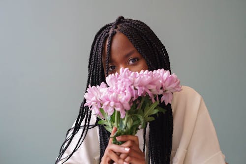 Black woman with blooming Chrysanthemums on gray background