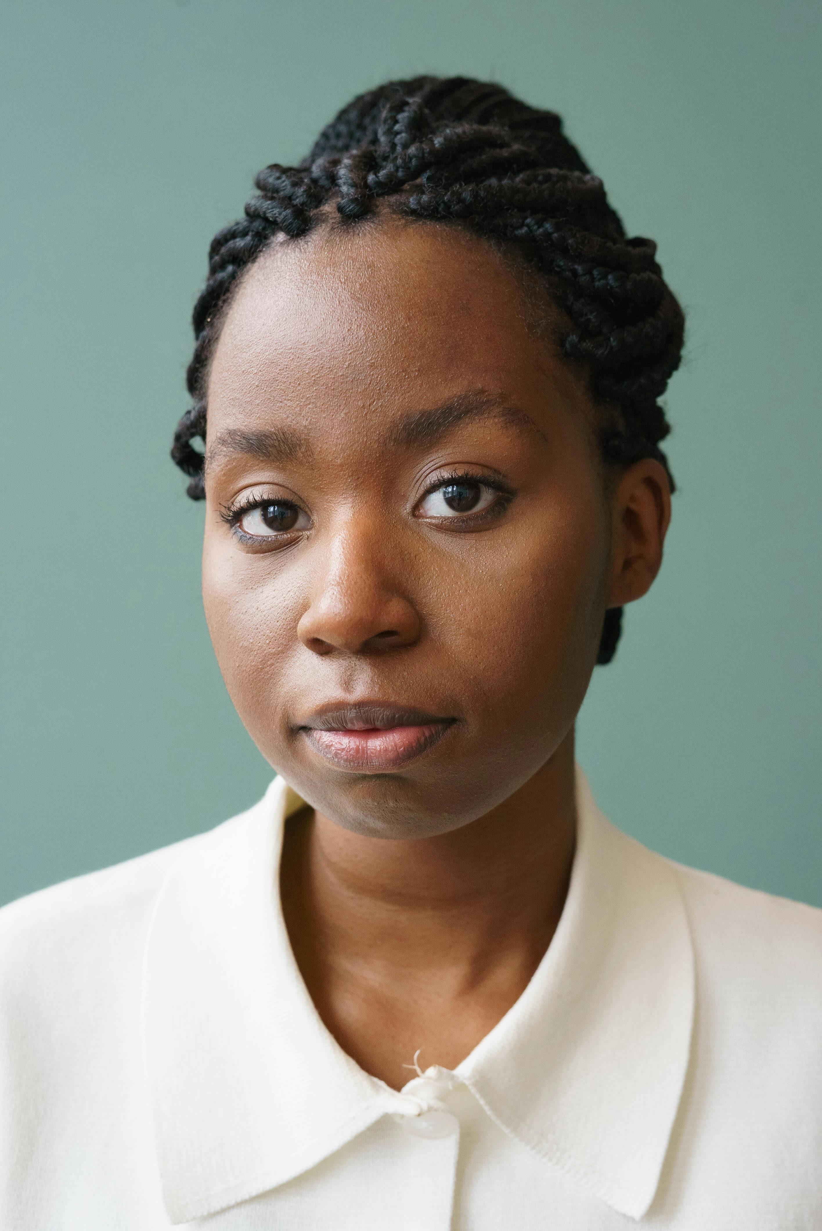Calm young African American female model with trendy braids i white shirt looking at camera against green background