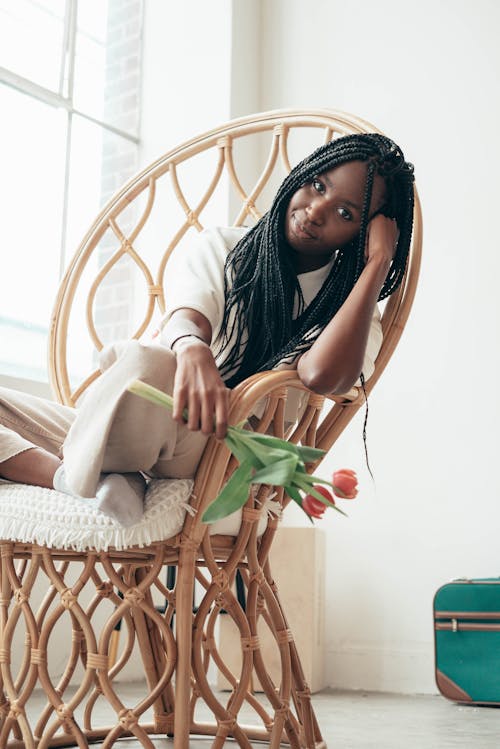 Free Dreamy young African American woman resting in bamboo armchair leaning on hand Stock Photo
