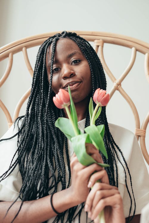 Smiling young black woman holding bunch of fresh flowers and looking at camera