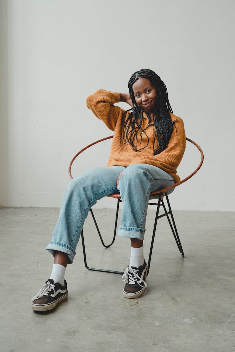 Happy Young Ethnic Female Millennial Sitting On Chair And Touching Hair